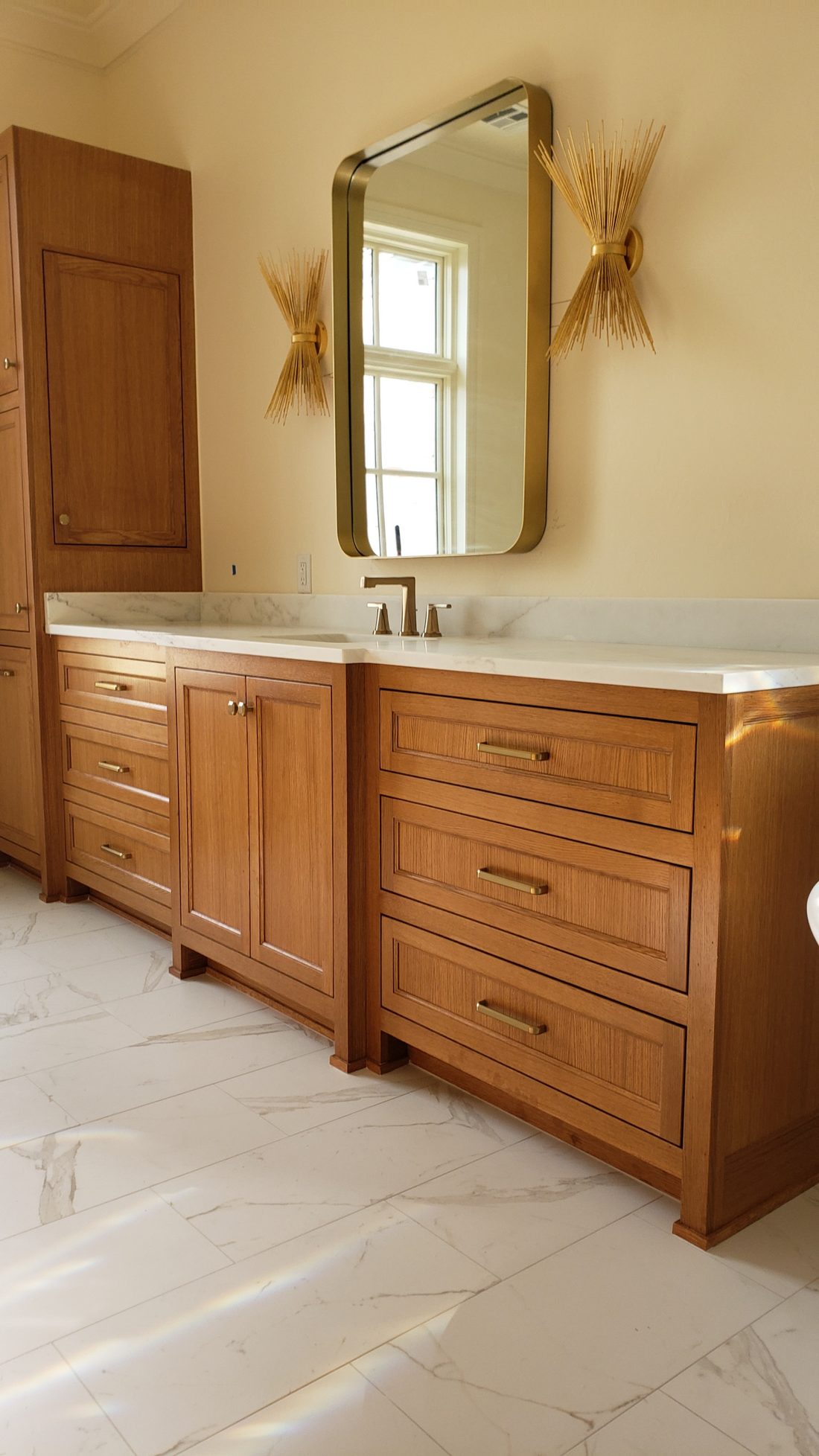 Natural oak bathroom vanity with brass hardware, a stone top and a brass-framed mirror