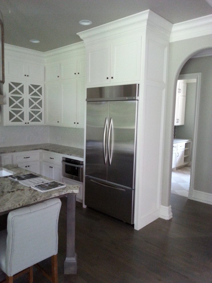 White kitchen with an integrated refrigerator surround, mullioned glass uppers and granite counters