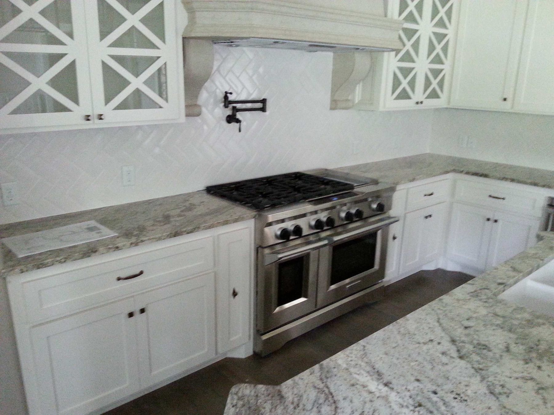 White painted kitchen with a herringbone tile backsplash, mullioned glass uppers and a professional range