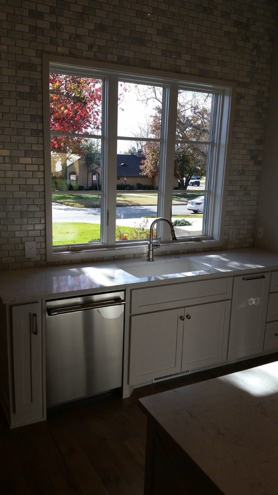 Kitchen sink run under a window with a brick backsplash and a dark stone counter