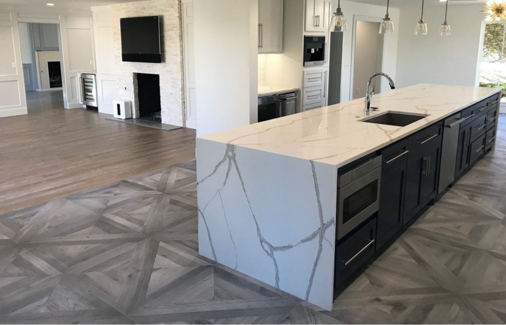 Open-plan kitchen with a long waterfall quartz island over navy cabinetry and parquet floors