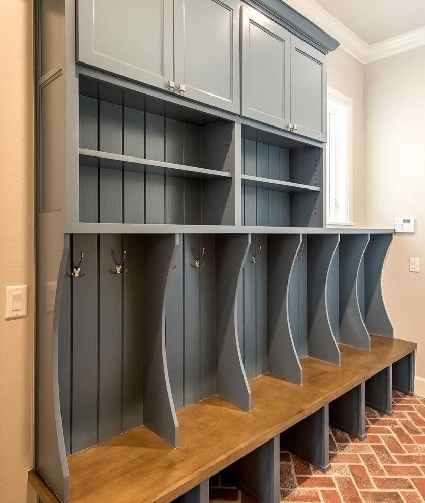 Blue-grey mudroom lockers with a bench, coat hooks and open cubbies over a brick floor